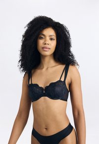 Svart spetsbh med genomskinliga koppar, delikat blommönster, justerbara band och en liten metallaccent i mitten. Slätt tyg i nederdelen.