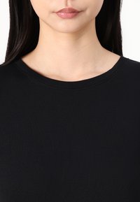 Top nero a coste con scollatura tonda, caratterizzato da una texture liscia e una vestibilità aderente. Nessun motivo o dettaglio prominente visibile.