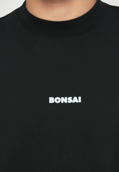 Zwarte katoenen t-shirt met een ronde hals en een witte bedrukte logo dat "BONSAI" in vetgedrukte letters op de borst zegt.