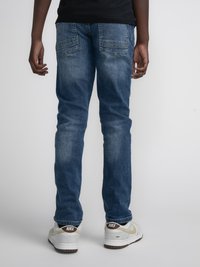 Jeans din denim într-o nuanță medie de albastru, cu o croială slim. Caracteristici includ două buzunare la spate, detalii pălite și o tiv curat. Purtați cu adidași albi.