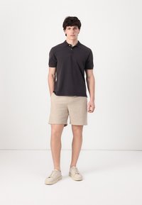 Mørk kortermet polo skjorte, beige linshorts og lyse joggesko. Enkelt design med myk tekstur og uformell passform.