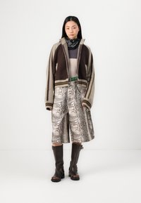 Knit zip-up cardigan in brown and beige, layered over a light top. Metallic snake-print shorts with pockets and brown knee-high boots.