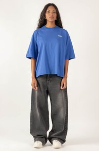 Blue oversized t-shirt made of cotton, featuring short sleeves and a crew neckline. Paired with loose gray jeans and white sneakers.