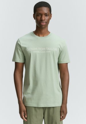 Vaaleanvihreä puuvillainen t-paita, jossa on pyöreä pääntie, lyhyet hihat ja etuosassa painatus "DENIM TOM TAILOR ESTABLISHED 2007".