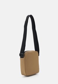 Bolso bandolera marrón con forma rectangular, hecho de tela suave, que cuenta con una correa negra y detalles de costura sencillos.
