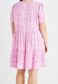 Růžové květinové šaty s krátkými rukávy, vybavené vícevrstvým designem a nařaseným pasem. Látka je pokryta drobným květinovým vzorem.