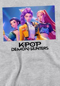 Light gray t-shirt featuring a graphic of three animated characters. Text below reads "K-POP DEMON HUNTERS" in bold black letters.