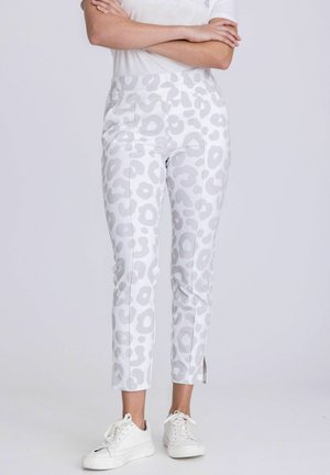 Witte slim-fit broek met lichtgrijze luipaardprint, enkelopeningen, gedragen met witte sneakers en een top met korte mouwen en gekruiste armen.