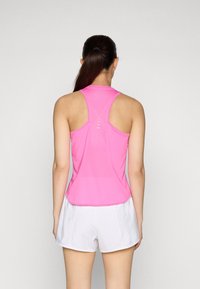 Różowy sportowy top na ramiączkach z designem typu racerback, charakteryzujący się siateczkową teksturą i białymi poziomymi paskami z tyłu. W połączeniu z białymi szortami.