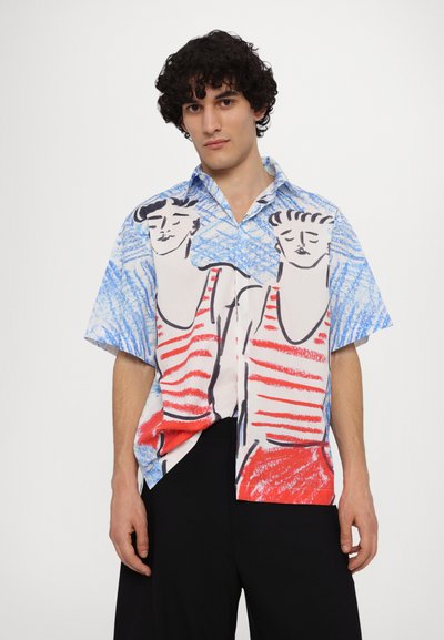 Camisa de manga corta con una colorida ilustración de dos figuras en rojo y azul, sobre un fondo blanco. La tela parece ligera y suave.
