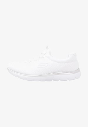 Chaussure de sport blanche avec un dessus en tricot texturé, un accent argenté sur la semelle et une semelle extérieure en caoutchouc flexible pour le confort et le soutien.