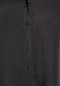 Čierna košeľa na gombíky vyrobená z hladkej tkaniny s jemným leskom, s okrúhlymi gombíkmi pozdĺž prednej strany a uvoľneným dizajnom goliera.