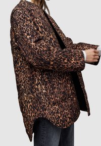 Kurtka w panterkę o luźnym kroju, z długimi rękawami, bocznymi kieszeniami i zaokrąglonym dołem. Wykonana z teksturowanej tkaniny w odcieniach brązu i czerni.