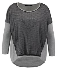Haut en maille noire avec un motif en losange, manches longues grises et encolure arrondie. Logo "Guess" en argent sur le triangle avant.