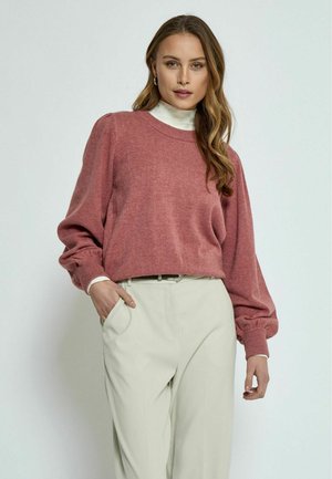Suéter de punto rojo con escote redondo y mangas abullonadas, combinado con pantalones de sastre beige claro. El suéter tiene una textura suave.