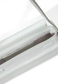 Bolso de mano de piel blanca con una textura lisa, una pequeña correa para el hombro y un único compartimento en el interior. Nombre de la marca grabado en un lado.