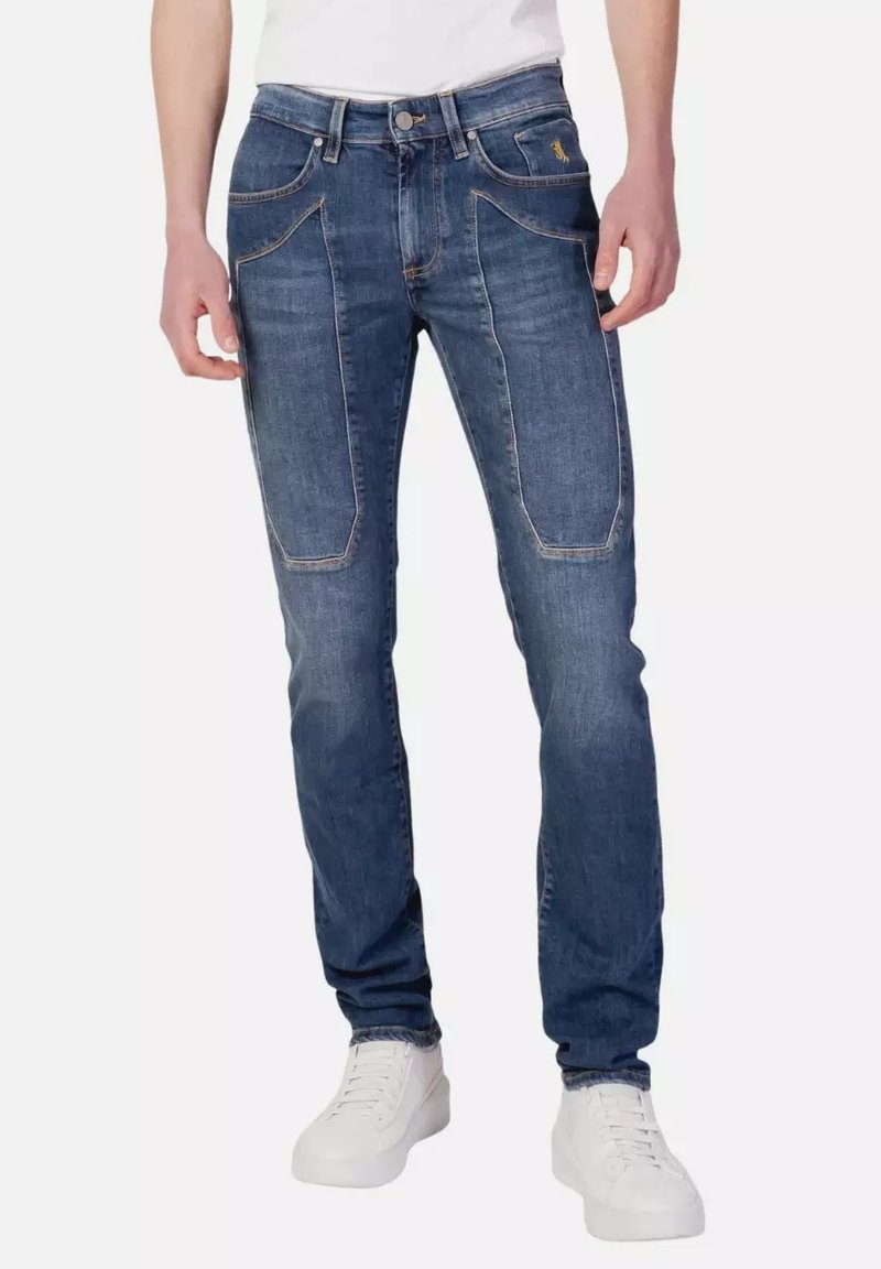 Jeans in denim blu scuro con una vestibilità slim, dotati di due tasche frontali e cuciture a contrasto. Indossati con sneakers bianche.