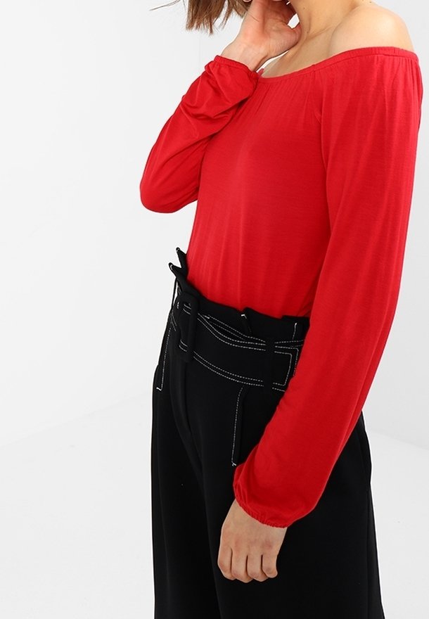 Rode off-the-shoulder top met lange mouwen, gemaakt van lichte stof. Gecombineerd met hoge zwarte broeken met contrasterende stiksels.