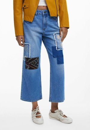 Light blue denim wide-leg jeans with frayed patches, featuring embroidered and patterned fabric accents on both thighs.