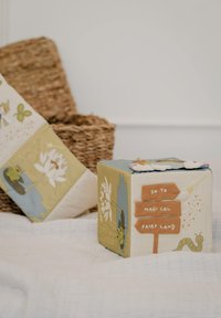 Kleurige stoffen kubus met speelse ontwerpen, waaronder een waterlelieblad, een wegwijzer en een rups. Zachte textuur met gestikte details.