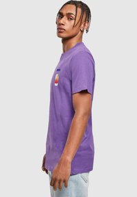 Camiseta de algodón morada, con cuello redondo y mangas cortas. Presenta un gráfico impreso de un atardecer en el pecho. Corte casual, textura suave.