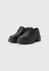 Chaussures brogue en cuir noir avec des détails perforés, bout arrondi, semelle épaisse à relief et design à lacets. Ajustement réglable avec œillets.