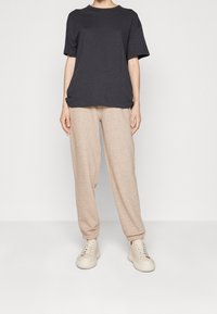 Ciemnoszara koszulka z krótkim rękawem w zestawieniu z jasnobeżowymi dresami i beżowymi trampkami. Prosty fason o luźnym kroju i miękkiej fakturze.