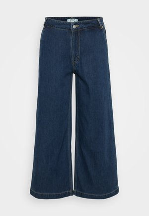 Calças de ganga de perna larga em azul escuro. Apresentam um fecho com botão, cinco bolsos, costura discreta e uma textura suave.