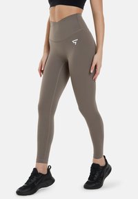 Hoge taille leggings in een taupe kleur, gemaakt van rekbaar materiaal, met een naadloos ontwerp, zwarte accenten en een logo nabij de heup.