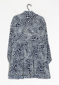 Vestido de manga larga en azul marino y blanco con un patrón de corazones, que presenta un dobladillo con volantes en capas y un corte holgado, colgado en un gancho negro.