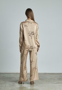 Set di loungewear in satin beige con decorazioni floreali, camicia a maniche lunghe con bottoni e pantaloni a gamba larga con una texture liscia.