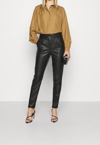 Brun silkblus med knappfram och puffärmar, matchad med högmidjade svarta faux läderbyxor och svarta remmar.