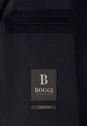 Interno di giacca blu scuro che mostra un'etichetta cucita con la scritta "B Boggi Milano" e una targhetta più piccola con la dicitura "100% lino" sotto una tasca.