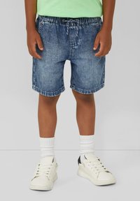 Shorts di denim con vita elastica e coulisse, in una lavatura blu sbiadita. Indossati con calzini bianchi e sneakers, mostrando un look casual.