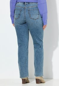 Jeans de mezclilla azul con un diseño de pierna recta, que cuentan con dos bolsillos traseros y detalles de costura visibles. Combinados con botas de tacón beige.