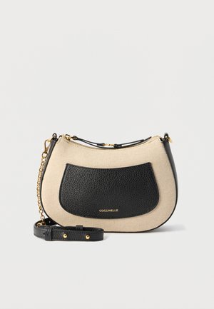 Lille beige stofhåndtaske med sort læder frontlomme, justerbar rem, guldkædedetalje og guldt brandlogo på lommen.