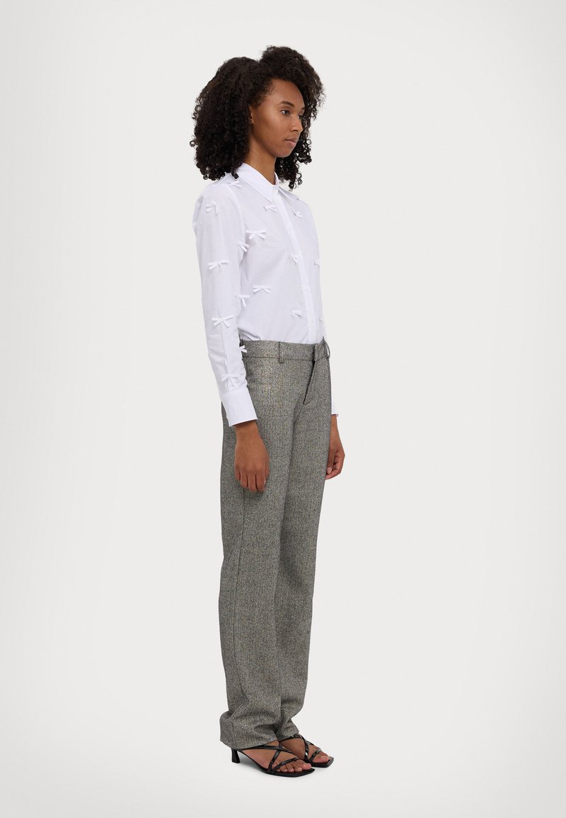 White shirt with bow accents, paired with gray patterned trousers and black strappy heels. The fit is relaxed and straight-legged.