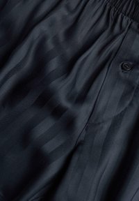 Tissu satin noir avec un léger éclat, présentant des rayures verticales subtiles, une taille élastique et un détail de bouton sur le côté.