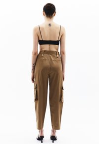 Bruine cargo-broek met hoge taille, twee zijzakken en twee achterzakken, gemaakt van een soepele stof. Gecombineerd met een zwart crop top.