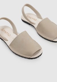 Sandalias de cuero beige con los dedos al aire, diseño sin hebillas y correa trasera. Suela de goma negra texturizada con detalles de costura visibles.