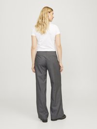 Pantalones de pierna ancha grises con un diseño a medida. Hechos de una tela texturizada, con un bolsillo trasero. Llevados con una camiseta blanca ajustada.