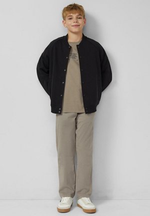 Czarna kurtka bomber, beżowy t-shirt z nadrukiem, khaki spodnie i białe sneakersy z gumową podeszwą. Casualowy, luźny krój całego stroju.