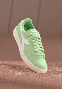 Sneaker verde in suede con accenti bianchi, punta rotonda, perforazioni sulla tomaia e lacci piatti. Suola testurizzata e collare imbottito.