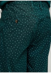 Groene gebloemde broek met een klein bloemenpatroon, gemaakt van zacht stof, met twee achterzakken en een knoopdetail.