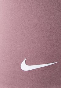Nike aktivna odjeća od svijetlo ljubičaste tkanine s glatkom teksturom, s istaknutim bijelim logotipom na donjem desnom dijelu.