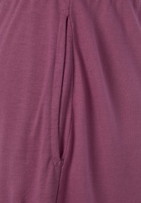 Purple fabric with a smooth texture featuring a side pocket opening and a discreet seam detail, indicating casual pants design.