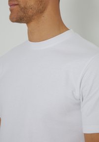 Camiseta de algodón blanca con cuello redondo, mangas cortas y un acabado texturizado, que resalta un diseño simple y clásico.