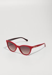 Red cat-eye sunglasses with gradient brown lenses. Features include a glossy finish, black patterned temples, and gold logo accents.