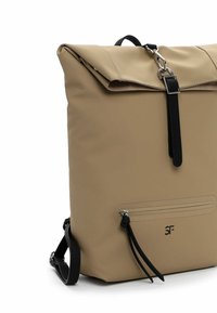Tan Rolltop-Rucksack aus strapazierfähigem Gewebe, mit einem schwarzen Riemen und silberfarbener Hardware, ausgestattet mit einer vorderen Reißverschlusstasche und einem Logo-Detail.