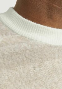 Lichtbeige trui met een zachte, fuzzy textuur. De halslijn heeft een ribbelige, witte rand, die het gezellige ontwerp van het kledingstuk benadrukt.